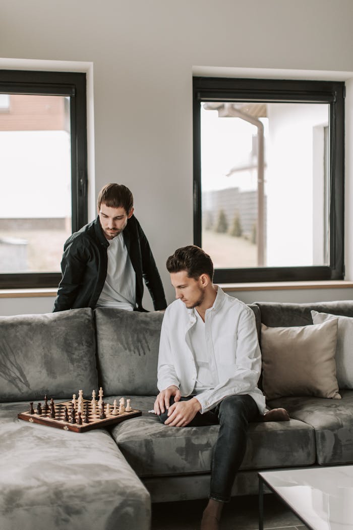 Man in White Long Sleeves Sitting on Gray Sofa Playing Chess